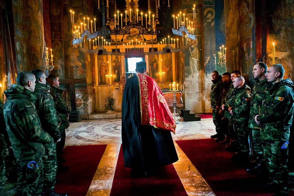 Orthodox priest is holding a Christmas service in the monastery of Visoki Decani in Kosovo, surrounded by the soldiers of KFOR who are in charge of protecting the monastery. Soldiers from different countries often attend services, although many of them are not Orthodox. Monastery was attacked from the nearby hills in 2000. and 2004. with a mortar, and several incidents were recorded in the recent past: In 2014 ISIS mark was left on the front gate and in January 2016 four armed men were arrested by Kosovo police in front of the monastery. They had rifles with ammunition and radical Islamist literature in the car.